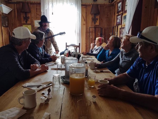 A man is playing a guitar while a group of people sit at a table