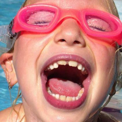 A young girl wearing pink goggles is swimming in a pool.