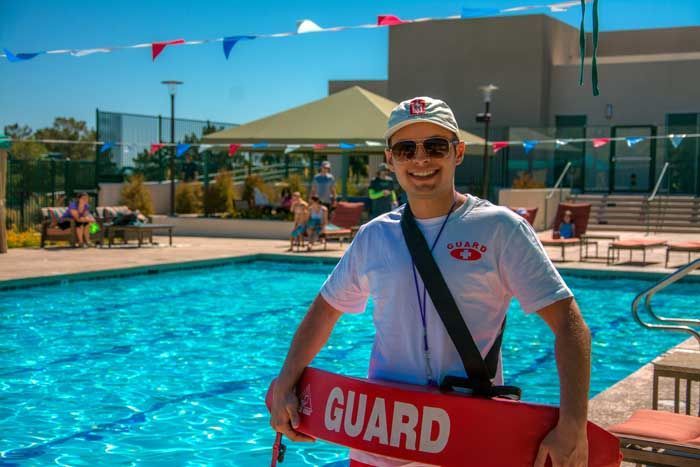 A lifeguard is holding a life preserver in front of a swimming pool.