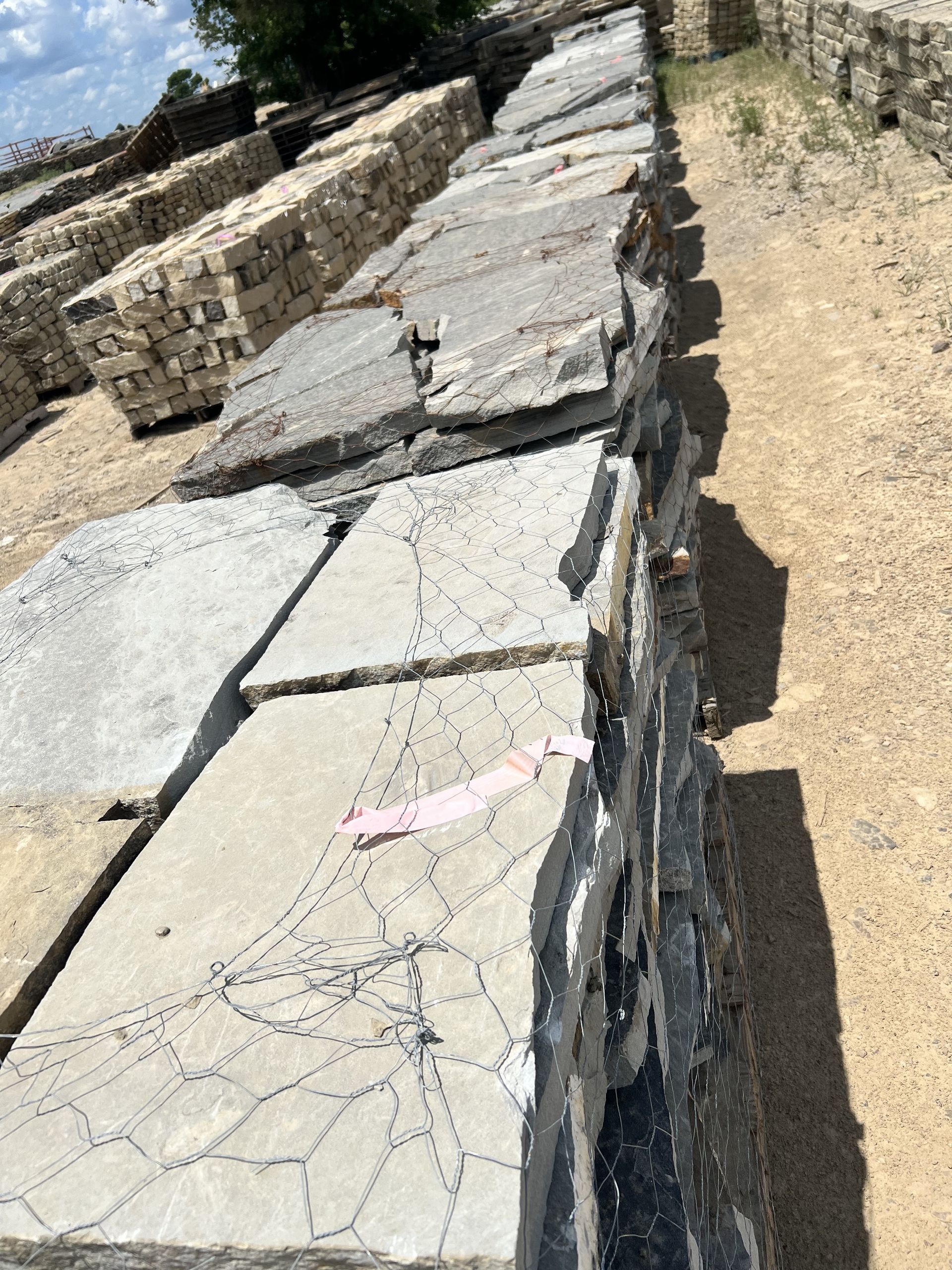 Stacked concrete slabs with crack patterns are lined up in an outdoor gravel storage yard.