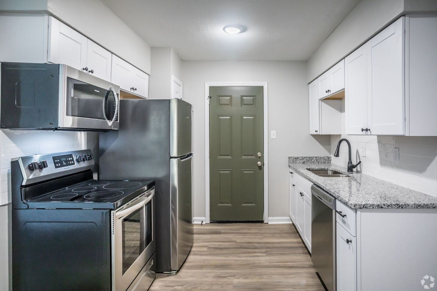 Modern kitchen with stainless steel appliances, white cabinets, granite countertops, and a green door.
