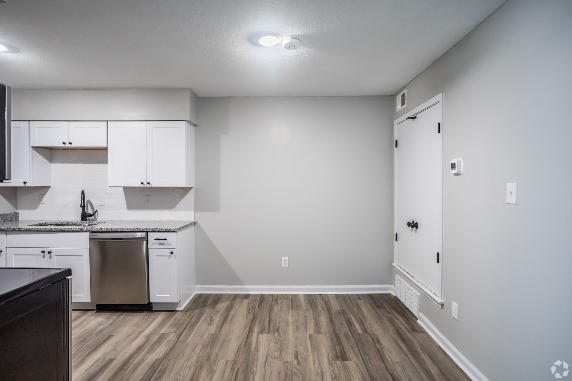 Empty kitchen with white cabinets, stainless steel appliances, and wood-look flooring.