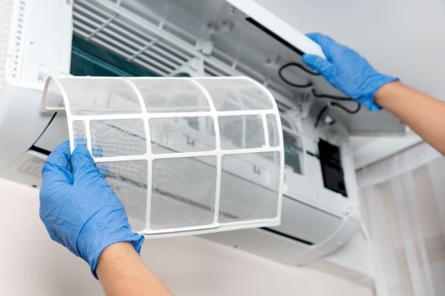 a person wearing blue gloves is cleaning an air conditioner .