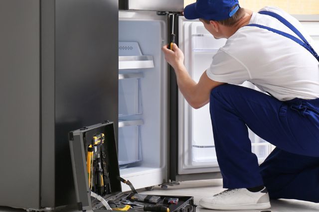 a man is repairing a refrigerator in a kitchen .
