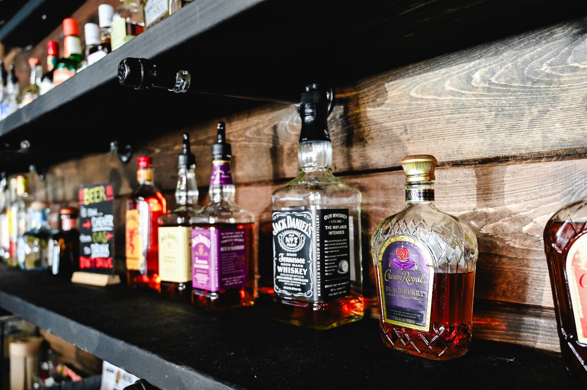 Row of liquor bottles on a bar shelf, with colorful labels and amber spirits under warm lighting