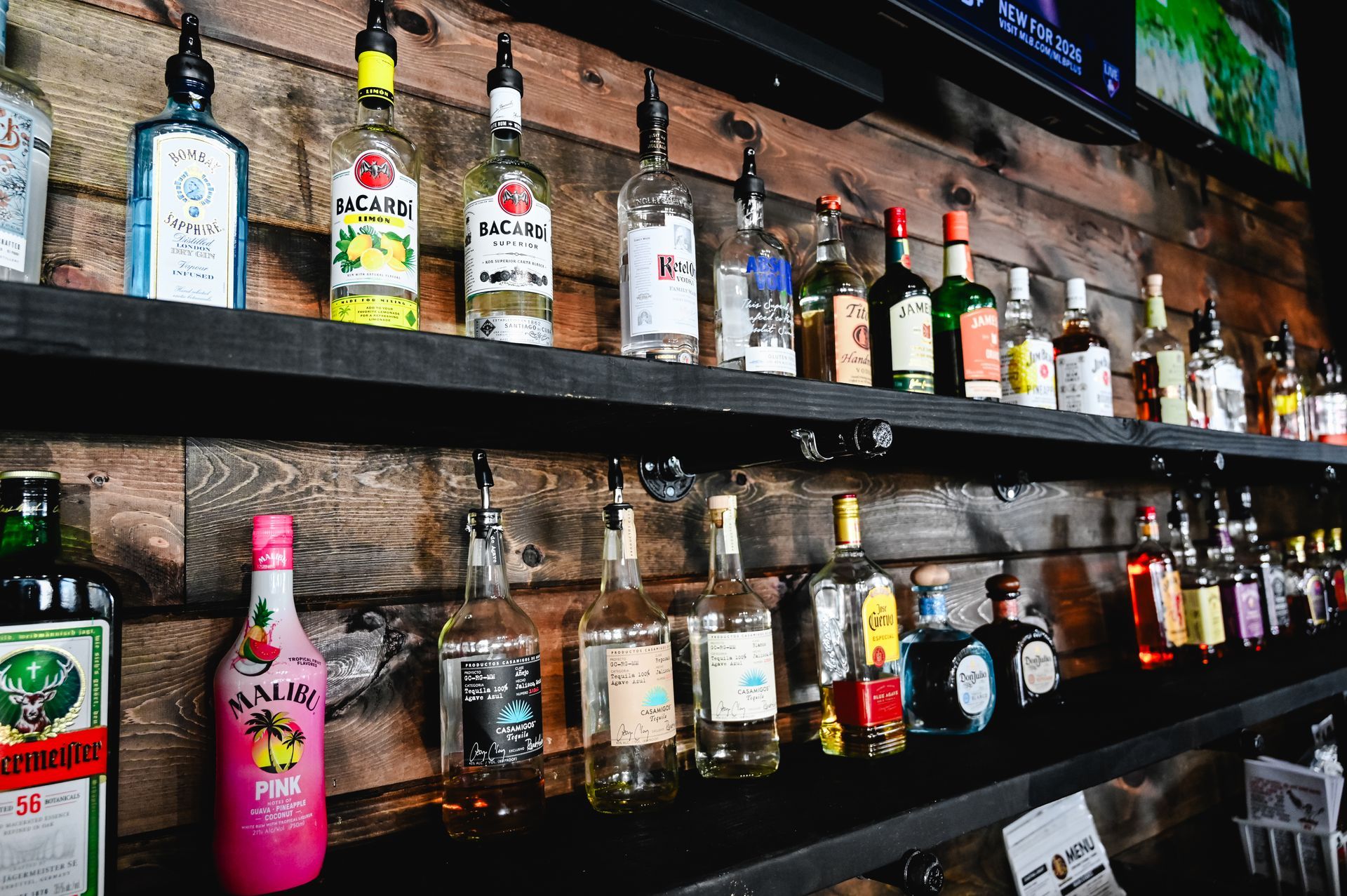 A row of bottles of liquor are lined up on a bar shelf.