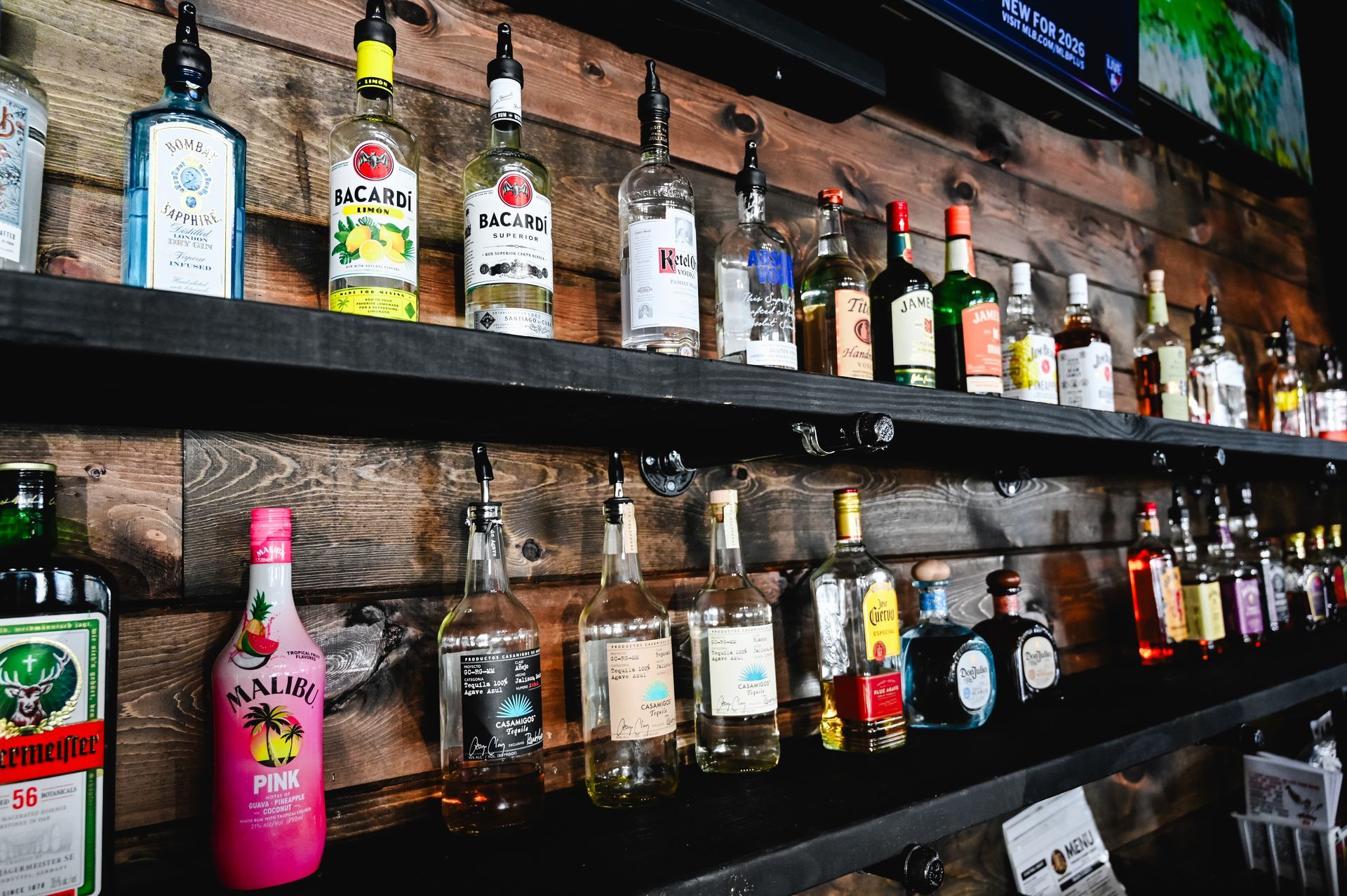 Many bottles of liquor are lined up on a shelf including jack daniels