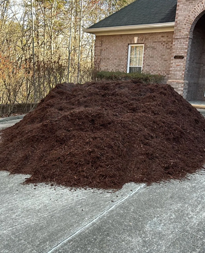 A large pile of mulch is sitting on the side of a road in front of a house.