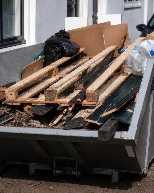Construction debris in a dumpster, with wooden planks and black trash bags.