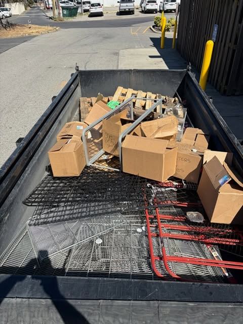 Cardboard boxes and metal mesh debris piled in a truck bed on a street at a curbside loading area