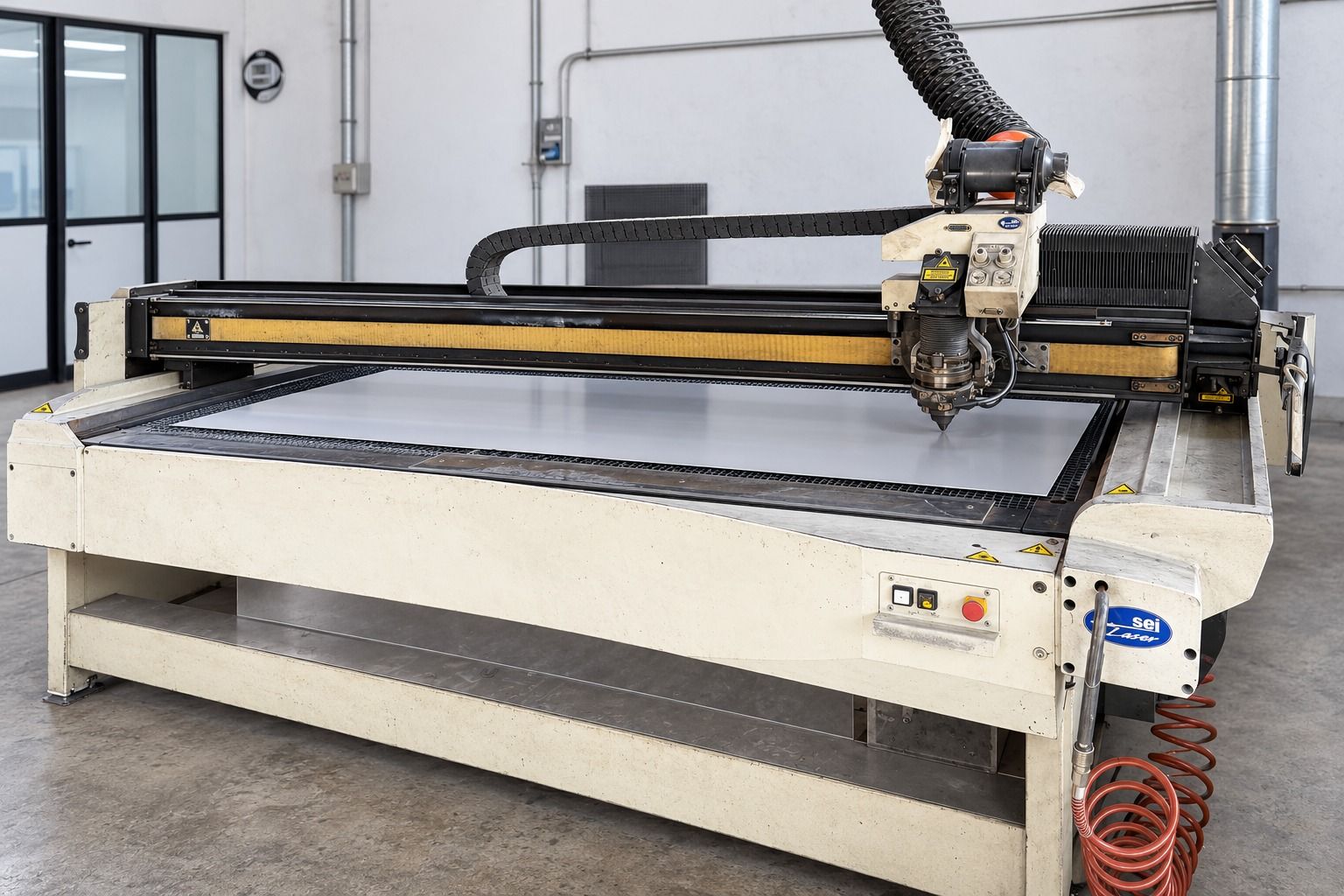 Grande macchina da taglio CNC in un'officina, con portale nero e base beige.