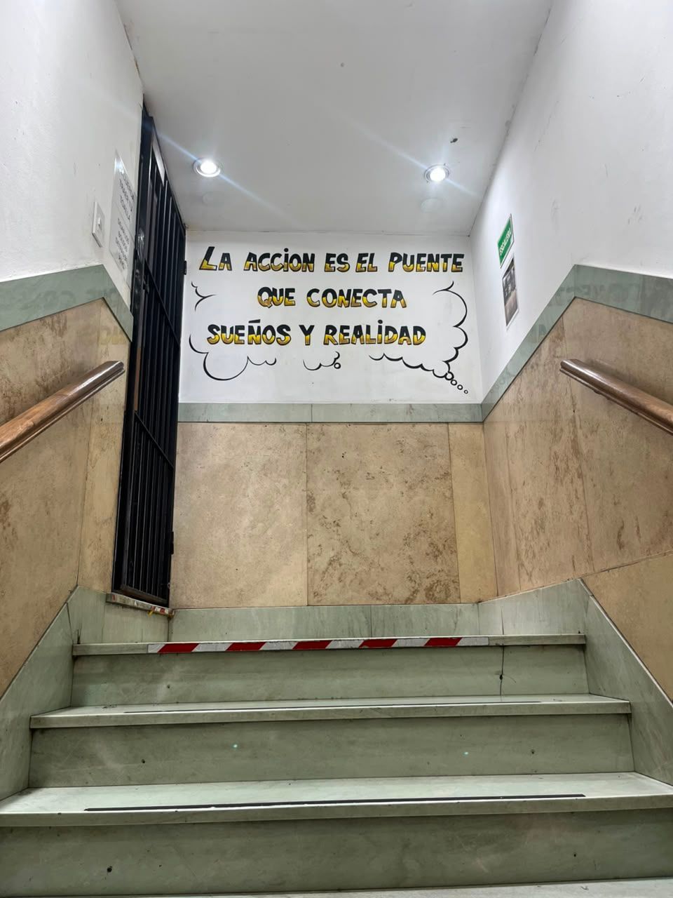 Stairwell with marble steps and Spanish wall sign reading “La acción es el puente entre el deseo y el vivir”