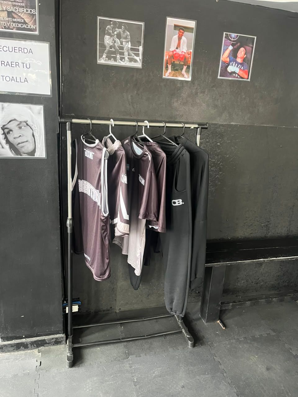 Un perchero con camisas moradas y negras contra una pared oscura, con pequeños carteles encima.