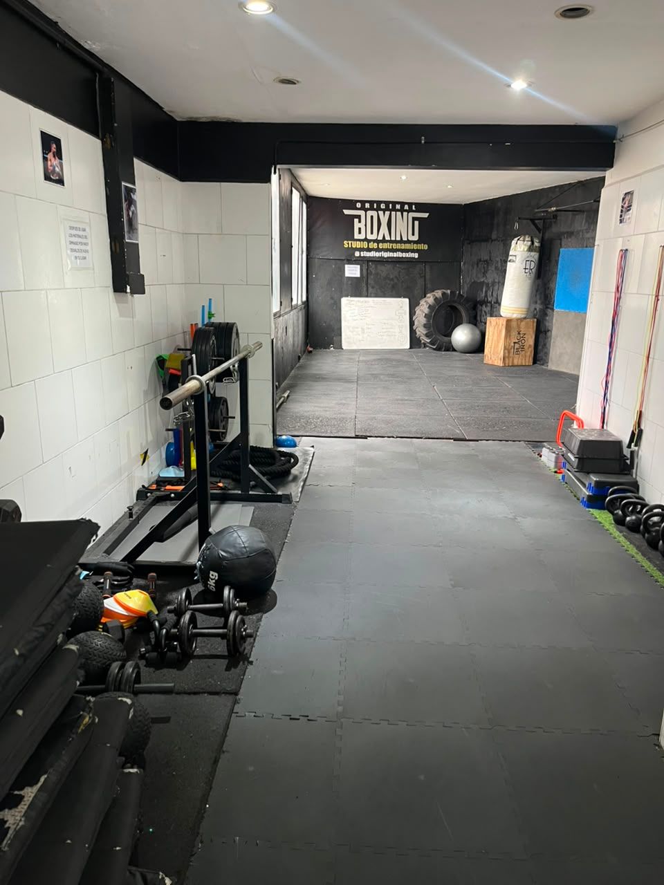 Gimnasio vacío con suelo negro, paredes blancas y aparatos de ejercicio a lo largo del lado izquierdo.