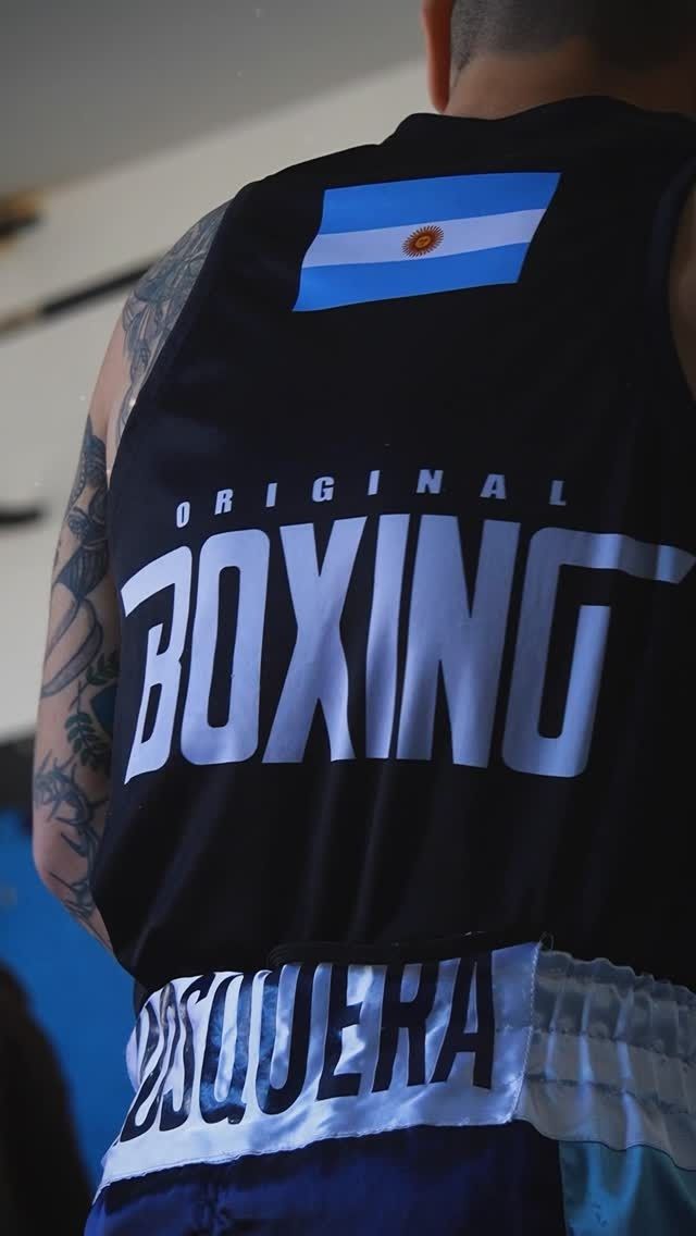 Vista trasera de un boxeador con una camiseta negra de “BOXEO” con un parche de la bandera argentina.