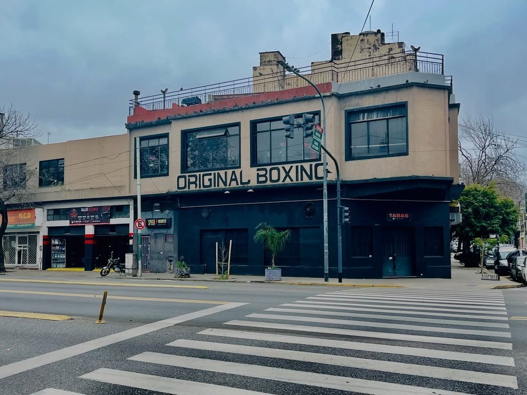 Vista de la calle de un edificio color canela con un letrero de “Original Boxing” y un paso de peatones enfrente.