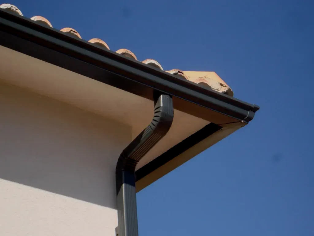 Coin de toit de maison avec une gouttière et une descente pluviale noires sur fond de ciel bleu