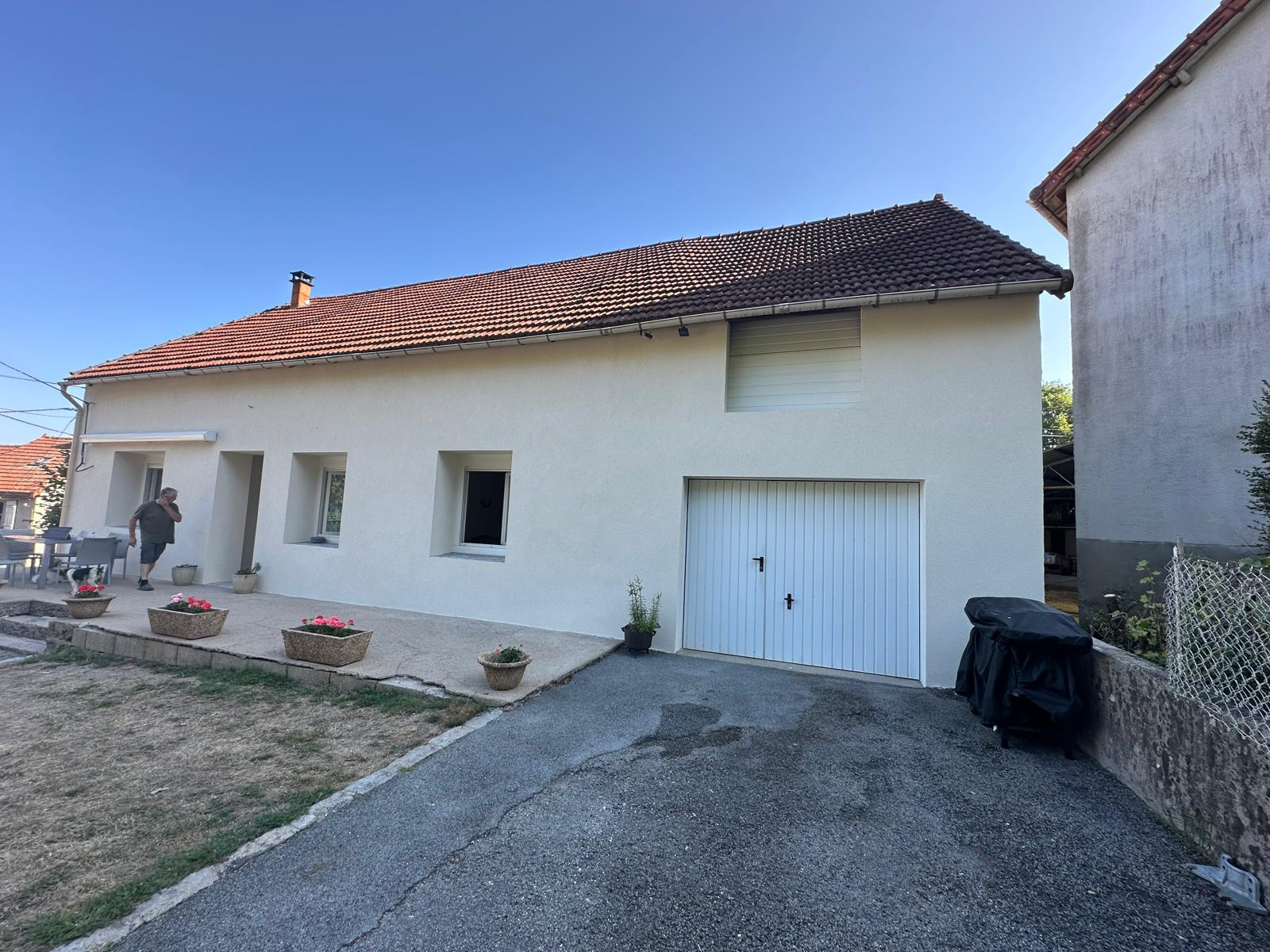 Maison blanche de plain-pied avec toit de tuiles rouges, garage, allée gravillonnée et petit jardin à l'avant.