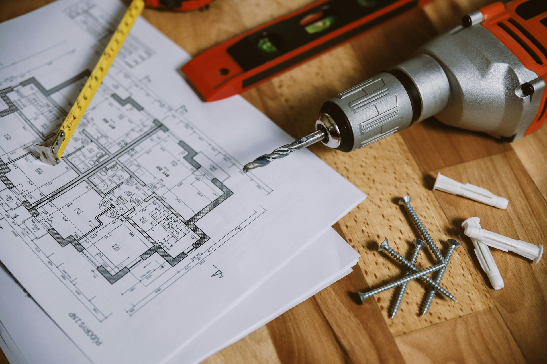 Perceuse, règle, crayon et vis sur un établi en bois au-dessus d'un plan de maison