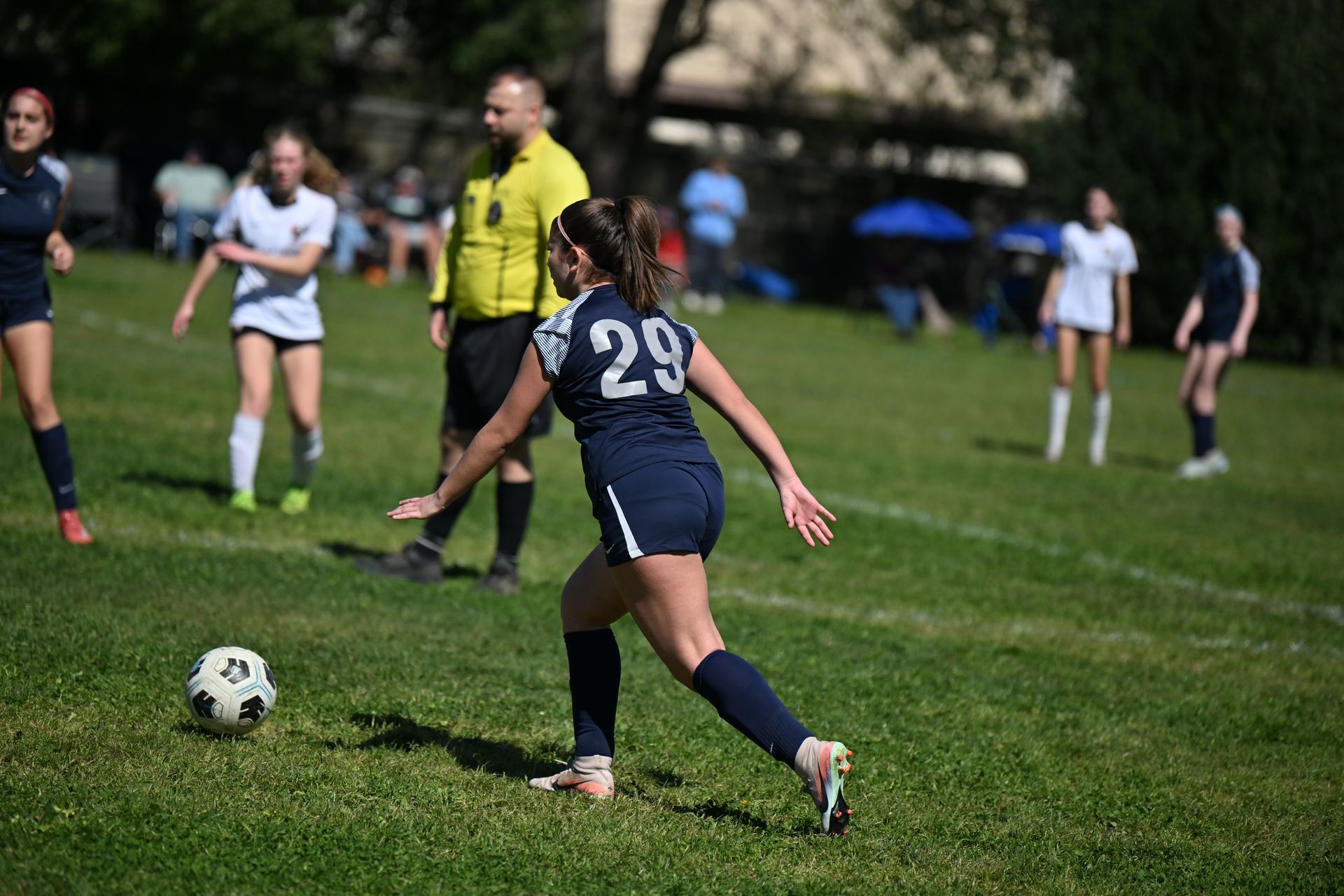 A soccer player in a blue uniform with number 29 dribbles a ball on a grass field near a referee in a yellow shirt.