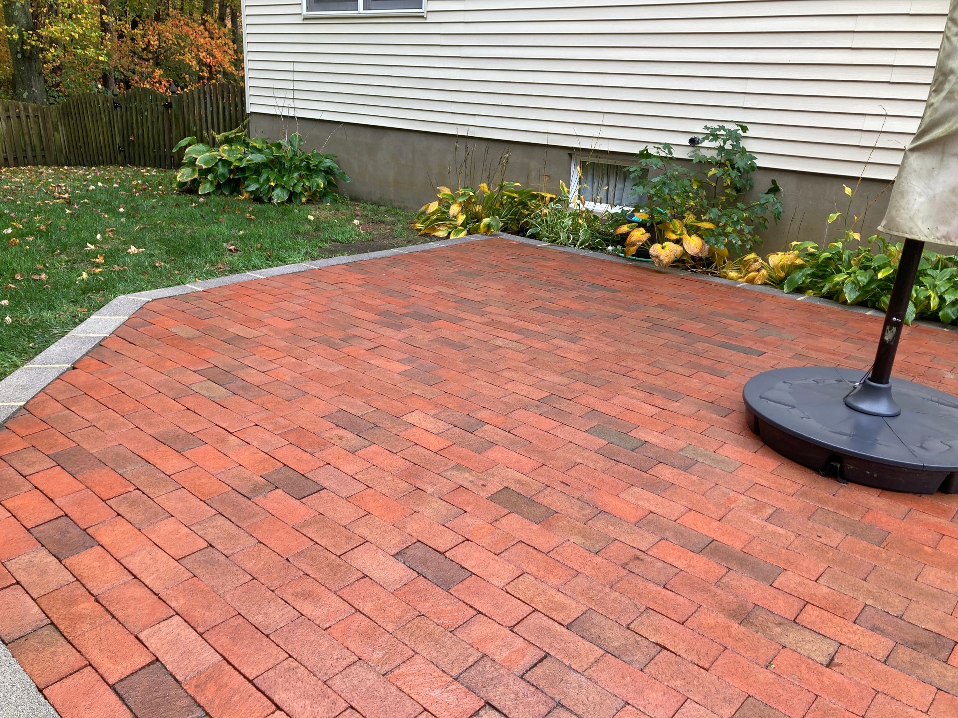A brick patio with an umbrella on it in front of a house.