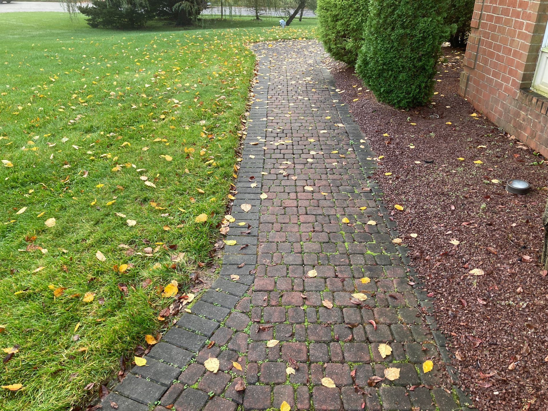 A brick walkway leading to a brick building next to a lush green field.