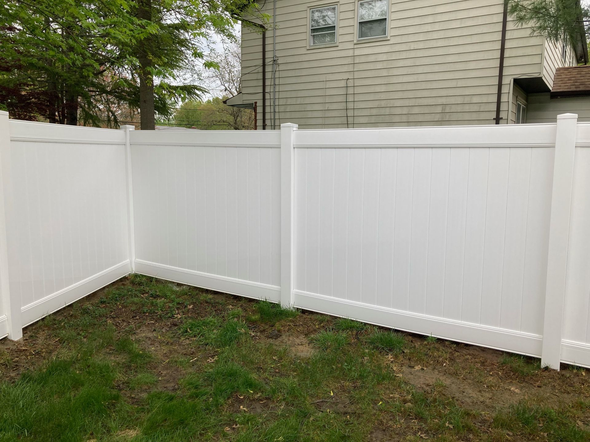 A white vinyl fence is in the backyard of a house.