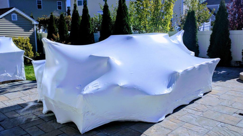 Outdoor furniture is wrapped in white plastic wrap on a patio.