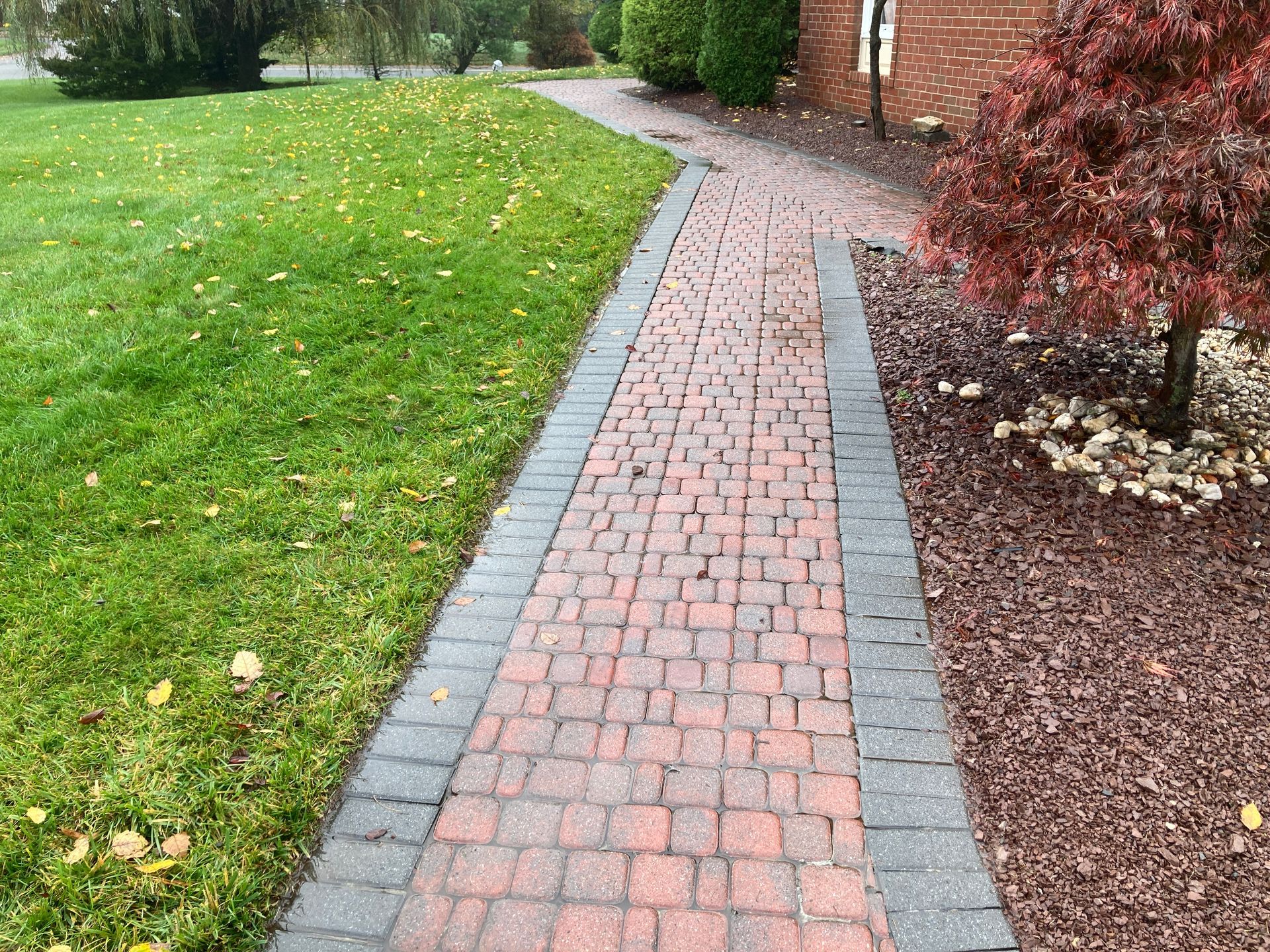 A brick walkway leading to a house next to a lush green field.