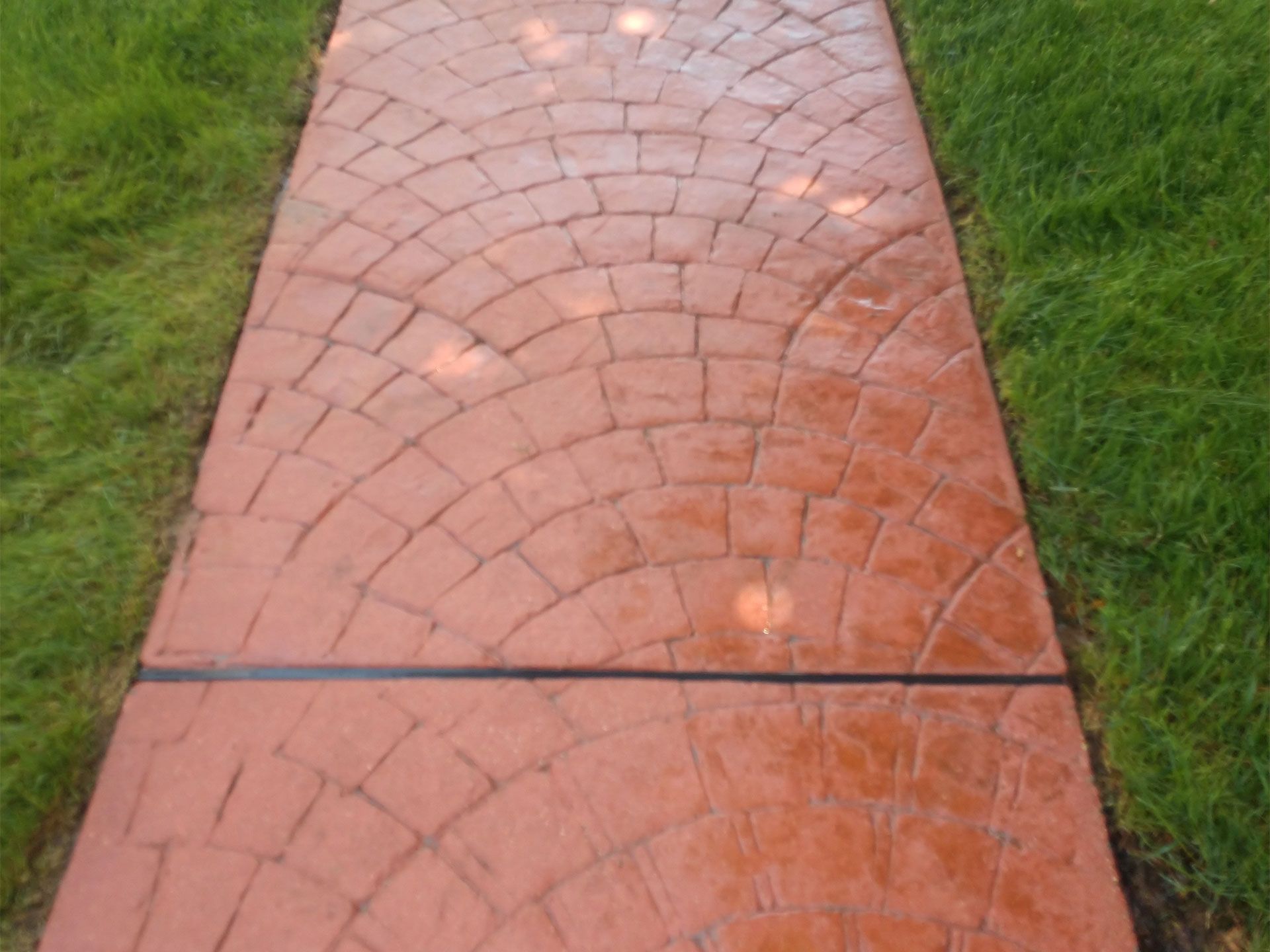 A red brick walkway leading to a lush green field.
