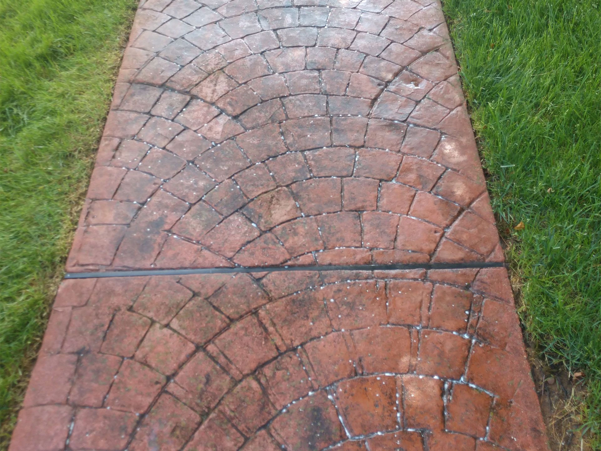 A brick walkway with a pattern on it is surrounded by grass.