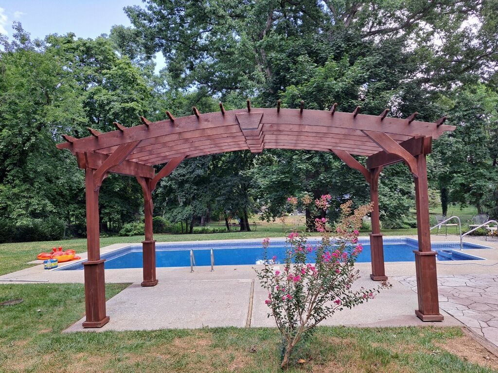 A wooden pergola is sitting next to a swimming pool in a backyard.