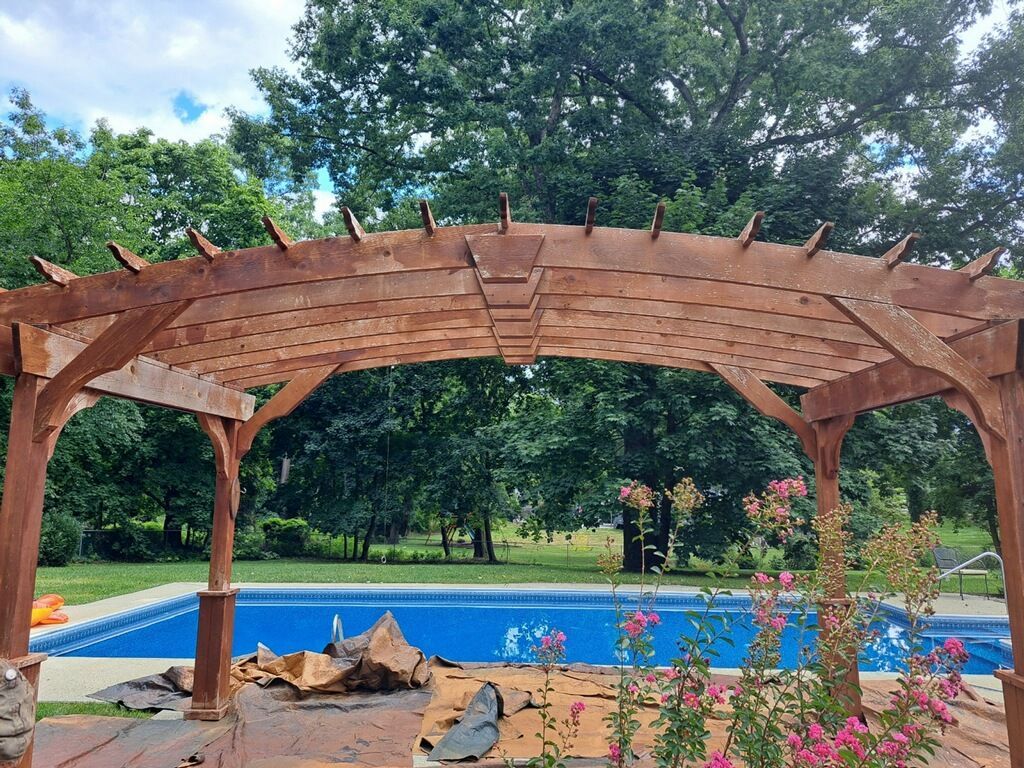 A wooden pergola is sitting next to a swimming pool.