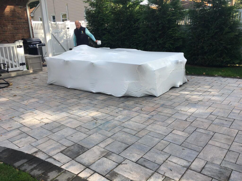 A man is wrapping a multiple pieces of furniture in shrink wrap on a patio.