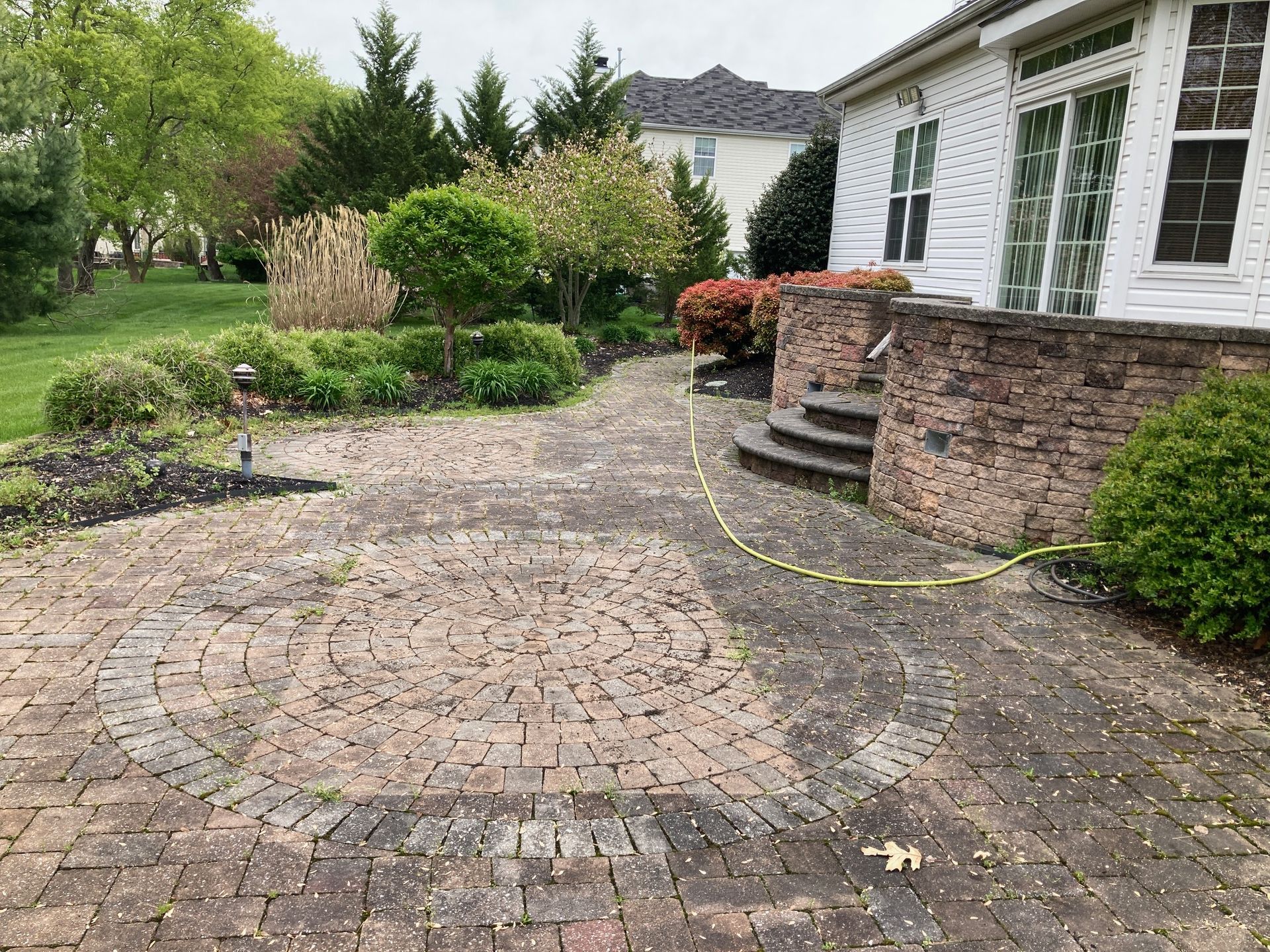 A brick walkway leading to a house with a hose attached to it.