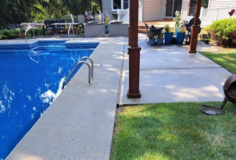 A large swimming pool is surrounded by a patio and a fire pit