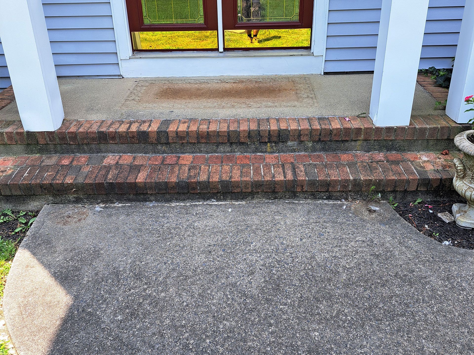 The front porch of a house with brick steps and a concrete walkway.