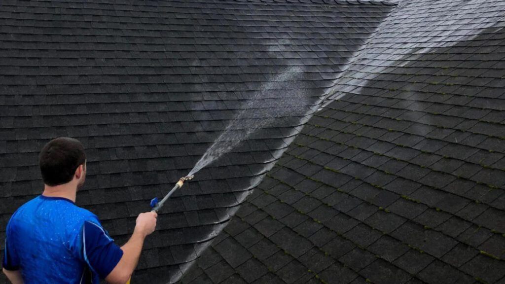 A man is cleaning a roof with soft wash cleaning pressure washer.