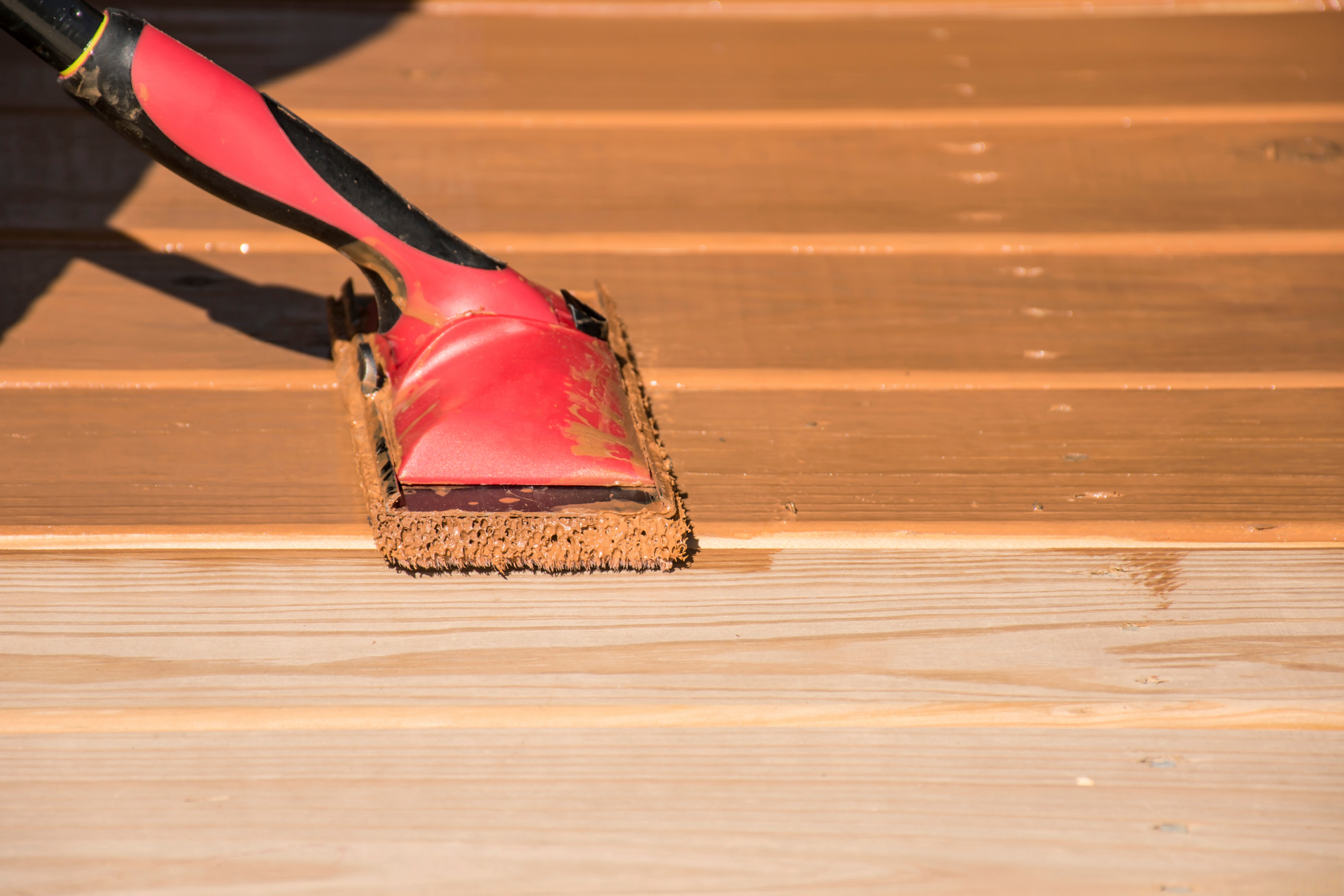 A person is staining a wooden deck with a paint pad.