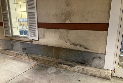A dirty wall with a window and shutters on it.