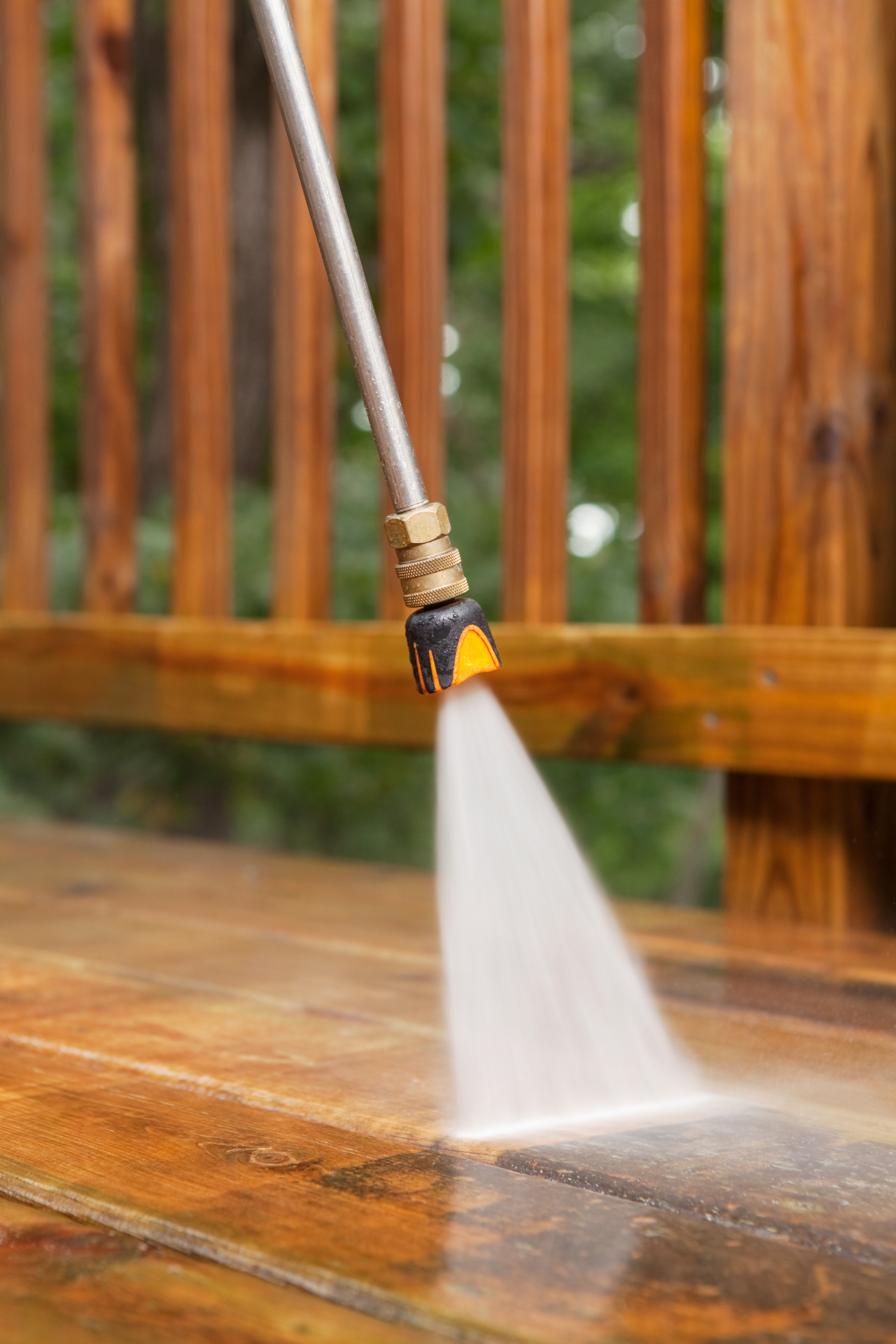 A person is using a pressure washer to clean a wooden deck.