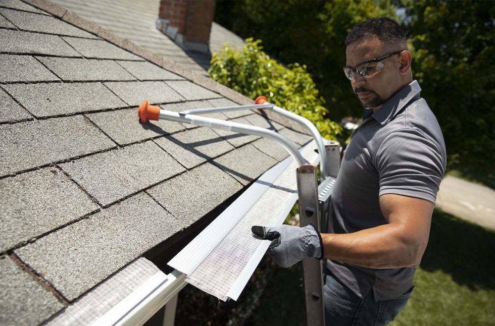 A man is standing on a ladder installing a gutter guard.