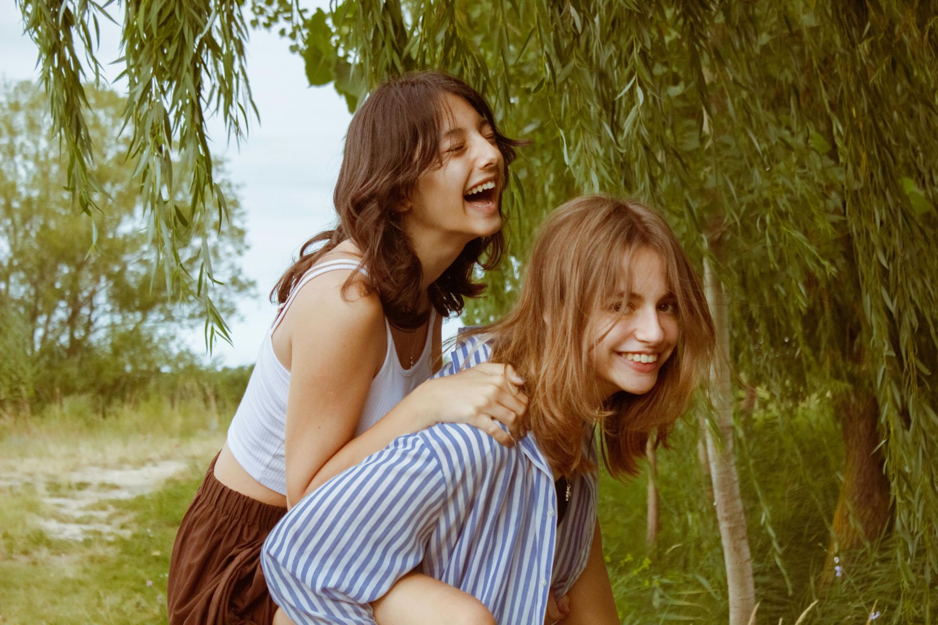 A woman is giving another woman a piggyback ride in a field in Middletown NJ.