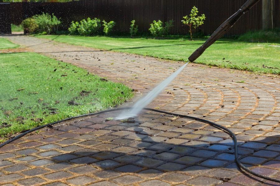 A person is using a high pressure washer to clean a brick patio.