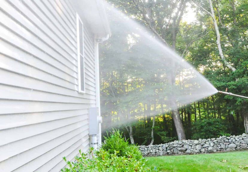 A man soft wash pressure washing the side of a house.