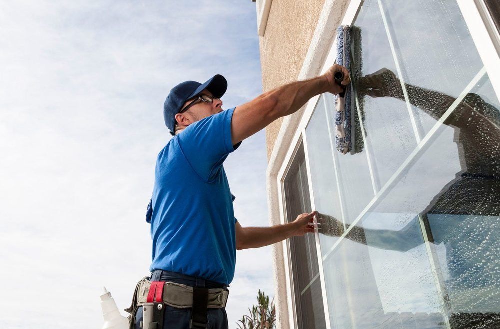 A man in a blue shirt is cleaning a window with a squeegee.