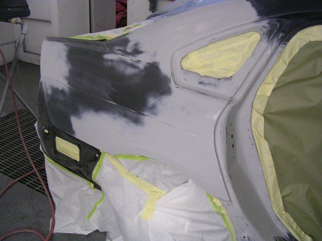 Partially primed car body with masked windows and sanding patches in an auto body shop