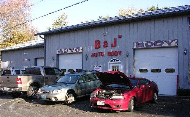 Auto body shop exterior with several parked cars, including a red car with its hood open.