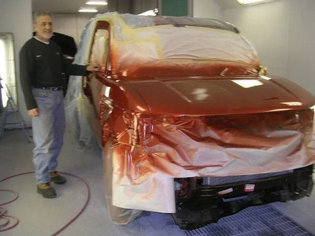 Car covered in red masking paper inside a paint booth, with a person standing beside it