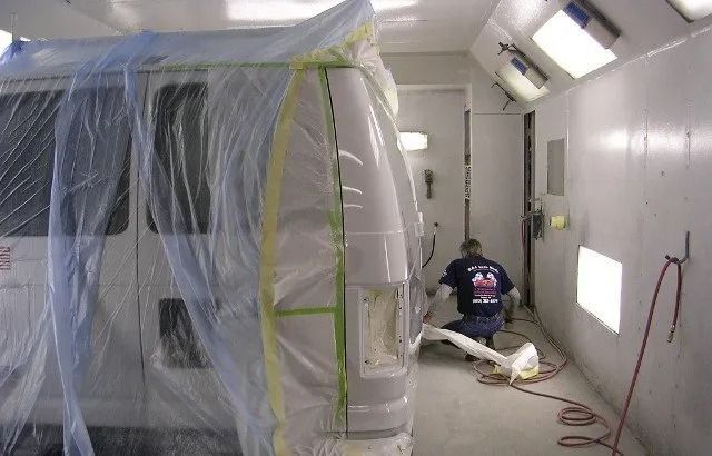 Worker masking a room for painting inside a plastic-covered hallway, with tools and dust protection setup.